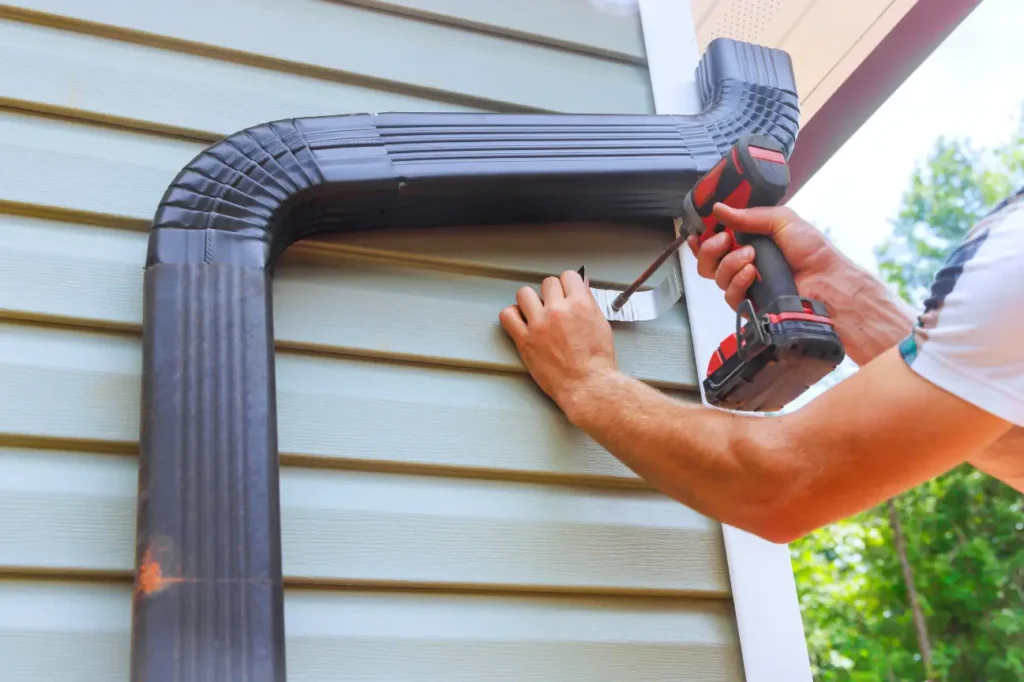 Worker installing a gutter and downpipe as part of plumbing services West Auckland for homes and businesses by Taylor Plumbing West Auckland